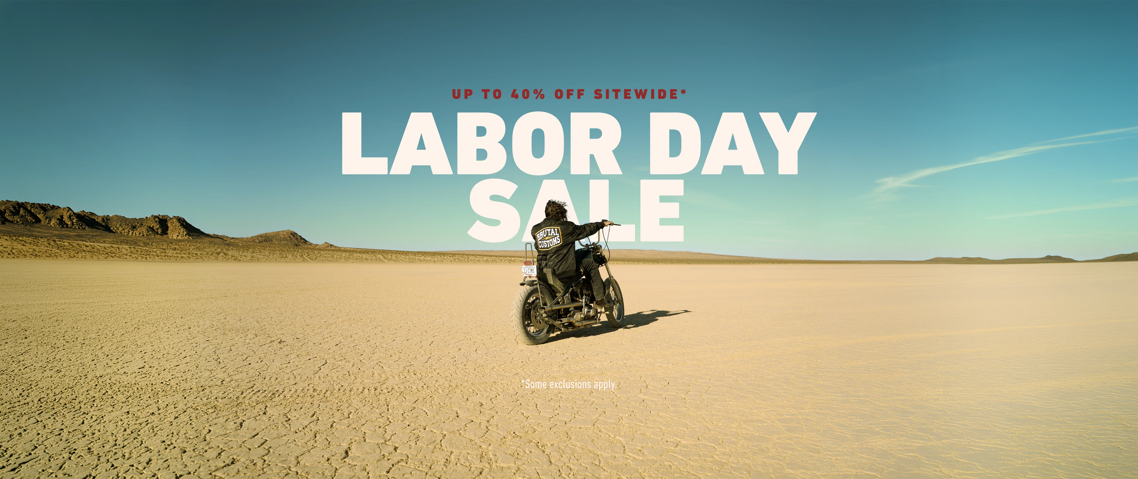 A promotional banner featuring a person riding a motorcycle across a vast desert landscape under a clear blue sky, with large overlaid text reading 'LABOR DAY SALE' and smaller text 'UP TO 40% OFF SITEWIDE'.